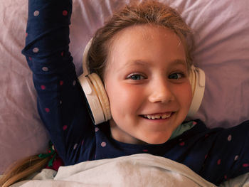 Child girl in headphones learns language listen to music podcast in smartphone online in bed at home