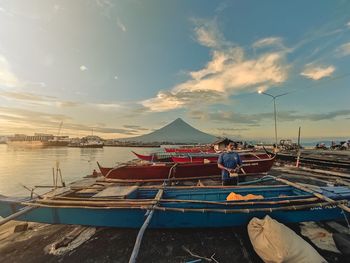 Man sitting on boat moored at beach against sky during sunset