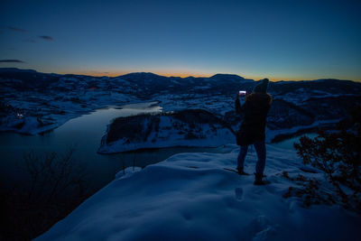 Rear view of person standing on snowcapped mountain against sky