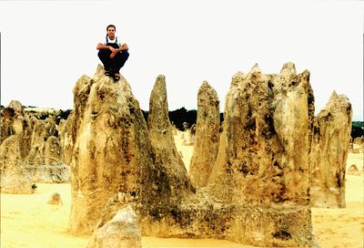 Person standing on rock formation against clear sky