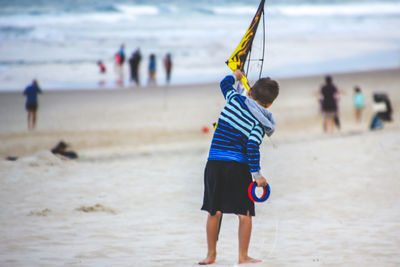 Rear view of boy holding kite while standing at beach