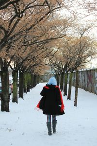 Rear view of woman walking on snow covered path amidst trees