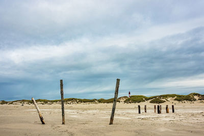 Wooden posts on sand against sky