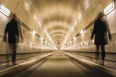 Rear view of man walking in illuminated tunnel