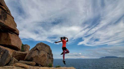 Woman jumping on rock against sea and sky