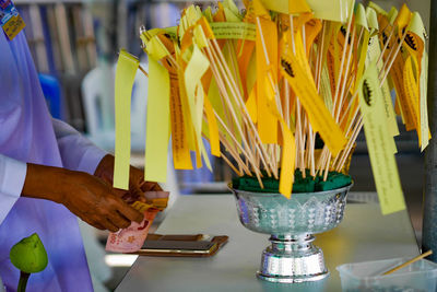 Midsection of person with yellow paper on sticks in container at table