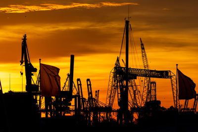 Silhouette cranes in harbour against sky during sunset