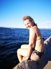 Young woman sitting on rock by sea against sky