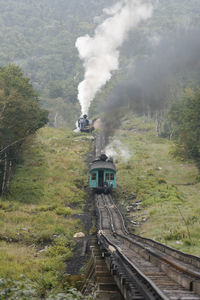 Two mount washington steam trains with passenger cars pushing up the summit.