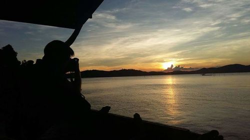 Silhouette man photographing sea against sky during sunset