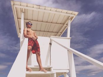 Low angle view of shirtless young man standing at lifeguard hut