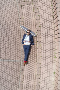 Businessman with skateboard lying on a wall using tablet and headphones