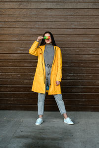 A girl in a yellow raincoat and a gray sweater holds a multicolored ice cream in her hand