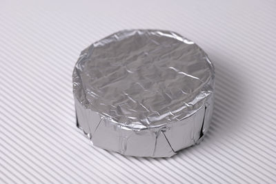 Round brie cheese in foil out over white corrugated background, close up.
