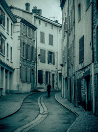 Rear view of man walking on street amidst buildings in city