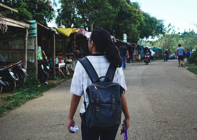 Rear view of woman with backpack walking on street in city