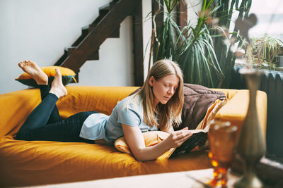 Woman reading book while lying on sofa at home