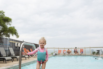 Portrait of girl standing at poolside against cloudy sky