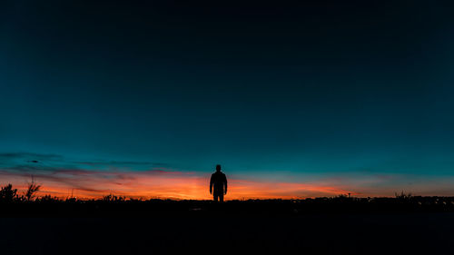 Silhouette man standing on field against sky during sunset