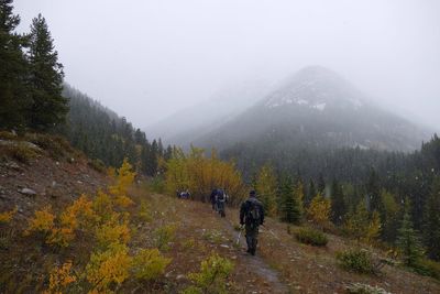 Rear view of hikers walking by mountains during foggy weather