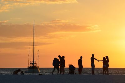 Silhouette of people standing on beach at sunset