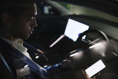 Businessman using smart phone sitting in electric car seen through window