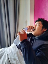 Young man drinking glass on bed