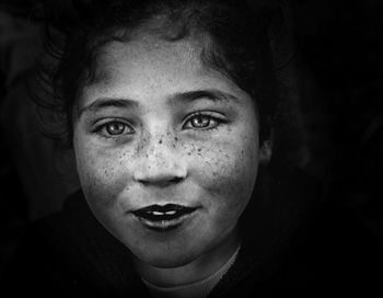 Close-up portrait of girl with freckles on face against black background