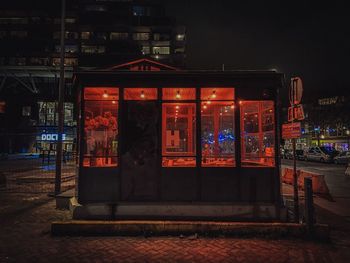 Illuminated street by buildings in city at night