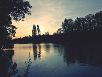 Silhouette trees by lake against sky during sunset