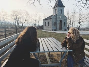 Female friends sitting on bench at field with building in background