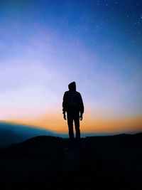 Rear view of silhouette teenage boy standing against dramatic sky during sunset