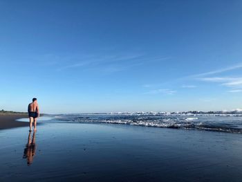 Rear view of shirtless man standing on beach against sky