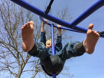 Low angle view of boy playing on jungle gym against blue sky at playground