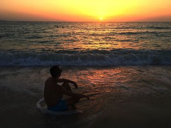 Rear view of man sitting at beach during sunset