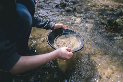 Low section person holding water in bowl at lakeshore