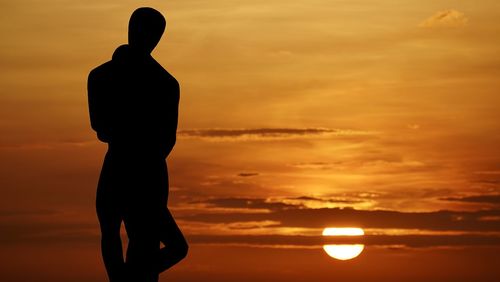 Silhouette man standing against orange sky