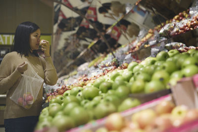 View of woman standing in supermarkets and choosing apples