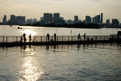 Silhouette people on riverbank against sky during sunset