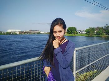 Smiling young woman standing on bridge against sky