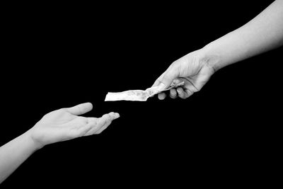 Close-up of hand giving money to friend over black background