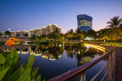 Illuminated buildings by river against sky in city