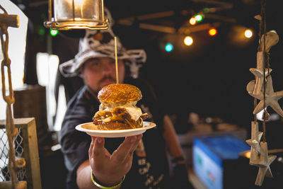 Portrait of mature man holding burger while standing at store