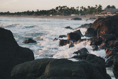 Waves breaking on rocks at beach against sky