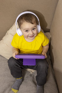 Little caucasian boy with yellow shirt playing game on digital tablet at home. 