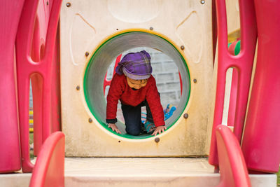 Full length of cute girl kneeling in outdoor play equipment in playground