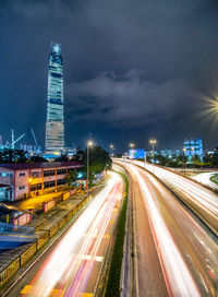 Light trails on road amidst buildings against sky at night