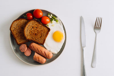 Breakfast plate with knife and fork on the white table, grilled sausage and whole wheat toast