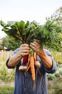 Man hiding face with vegetables in garden