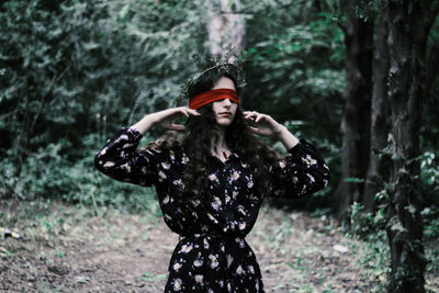 Fashionable young woman with blind fold while standing in forest